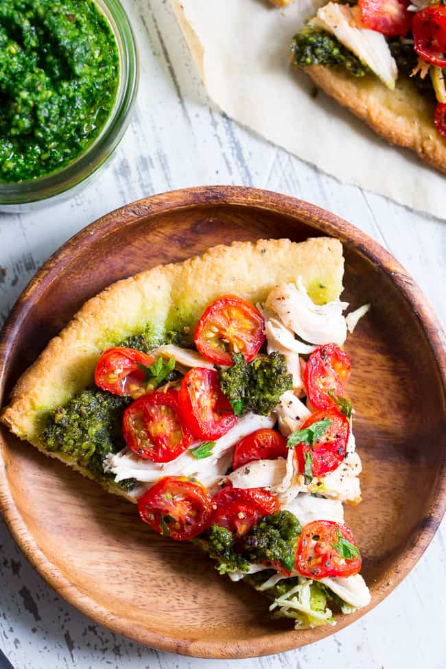 This simple chicken pesto pizza starts with the perfect quick and easy paleo pizza crust, topped with a flavor-packed dairy-free homemade pesto, shredded chicken and cherry tomatoes.  This fun meal great for dinner or lunch, is kid approved, grain-free, dairy-free and insanely delicious.