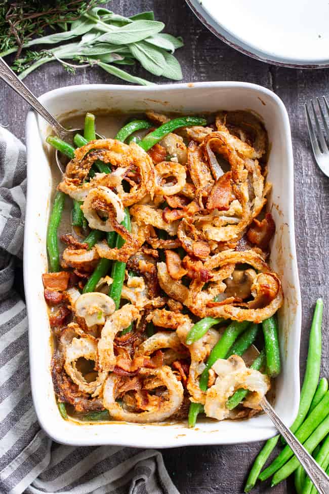 a white dish with green beans in a brown sauce topped with fried onions