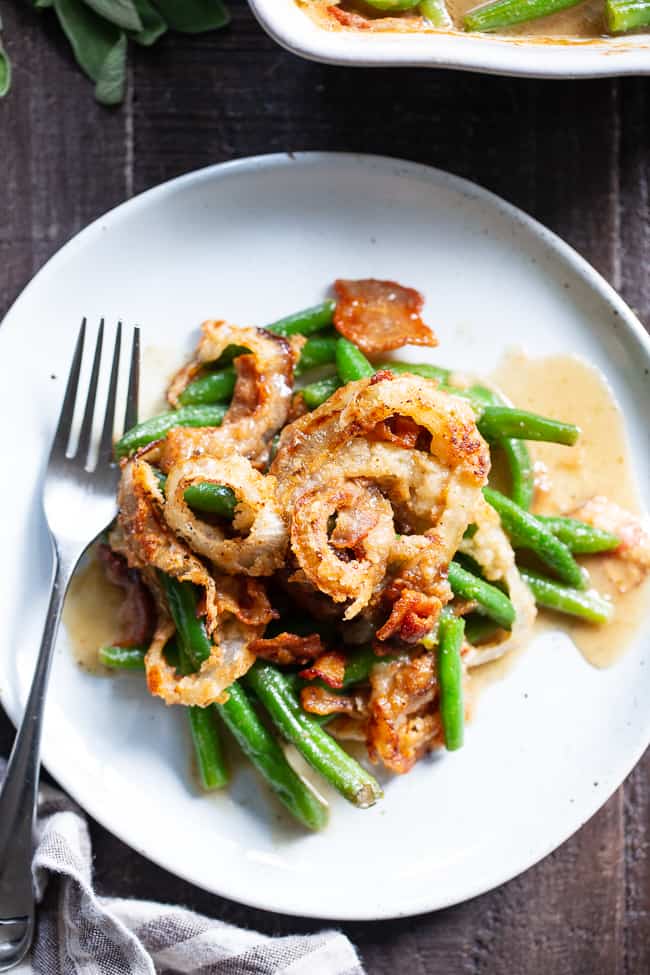 a serving of green bean casserole with fried onion rings on top all on a white plate with a fork