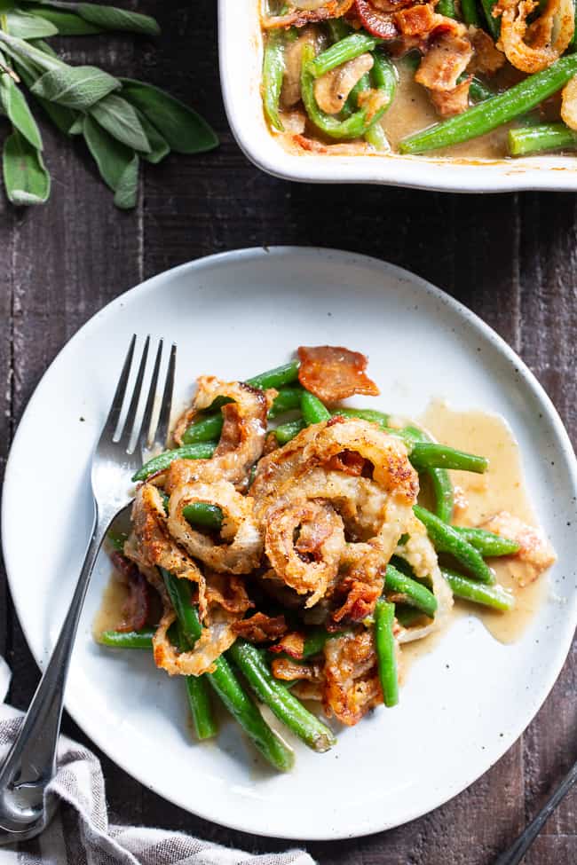 bright green bean casserole with onions and bacon on a white plate with a silver fork