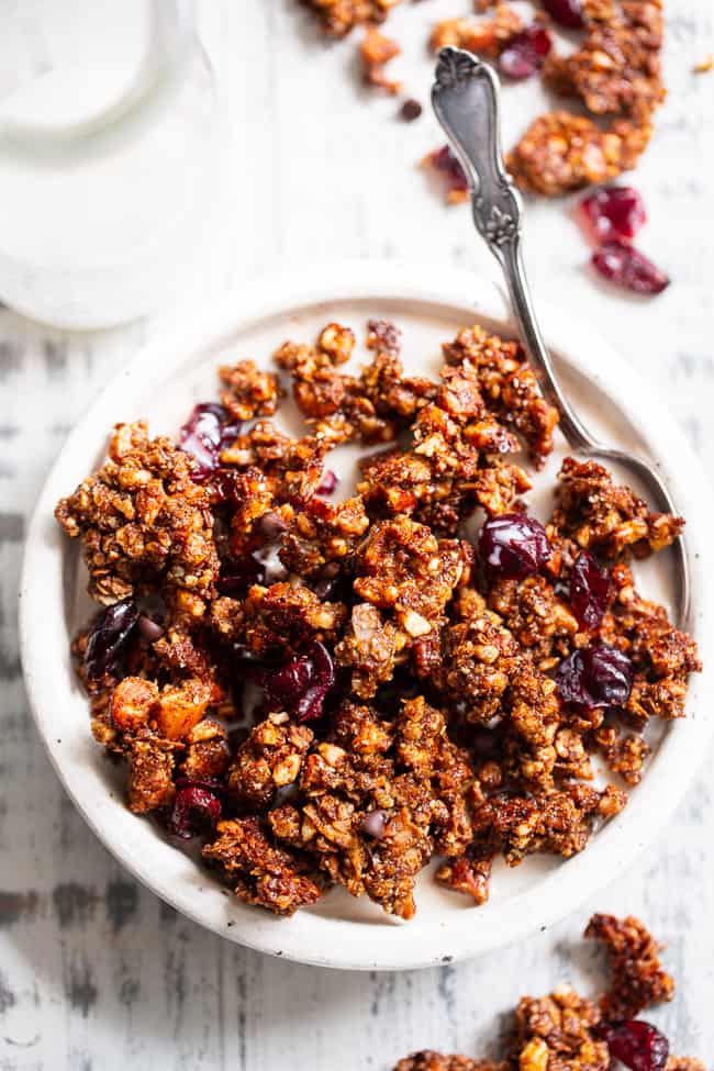 This Paleo gingerbread granola is perfect for snacking or breakfast! The crunchy granola clusters are sweetened with maple and molasses, baked until toasty, and mixed with sweet cranberries and dark chocolate chips.  Vegan, grain free, dairy free.