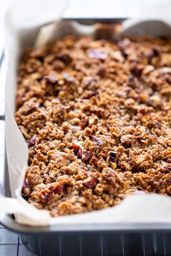 brown coffee cake with pecan crumble topping in a parchment lined gray cake pan