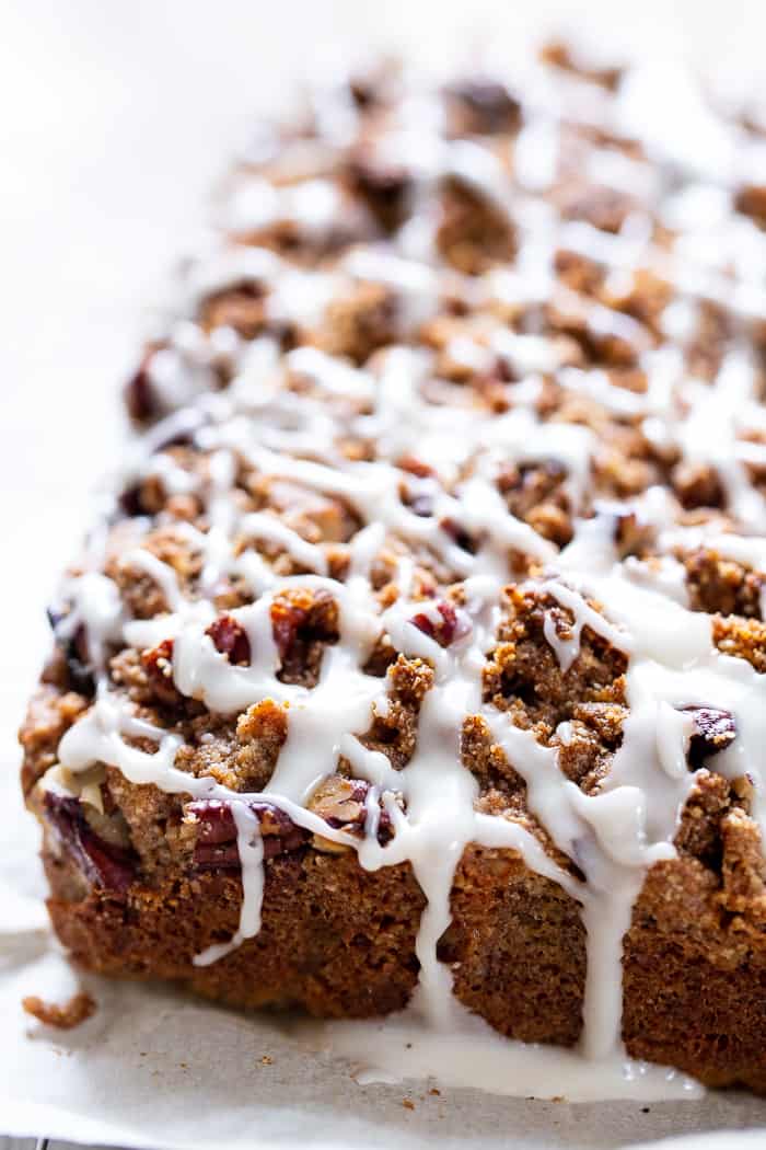 a brown cake loaf with crumbly topping and white frosting drizzled generously overtop