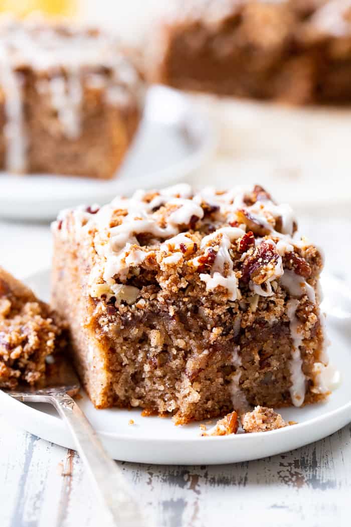 a slice of coffee cake with white drizzle on a white plate, a bite taken from the corner with a fork