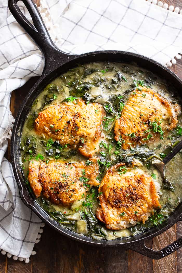 four cooked chicken thighs in a spinach artichoke mixture in a cast iron skillet 