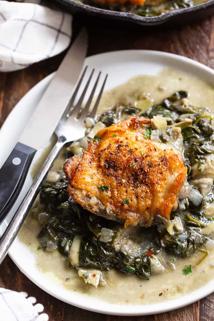 spinach artichoke chicken on a white plate with a knife and fork on the left side of the plate