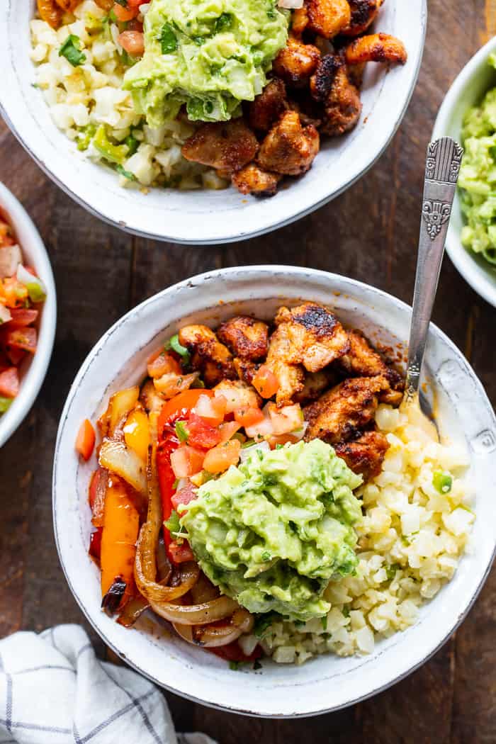 These Paleo Chicken Burrito Bowl are packed with tons of flavor and goodies!  Bite size seasoned chicken thighs, zesty cauliflower rice, pepper and onions plus and easy guac make these bowls healthy, filling, and a family favorite.  Whole30 and keto friendly.