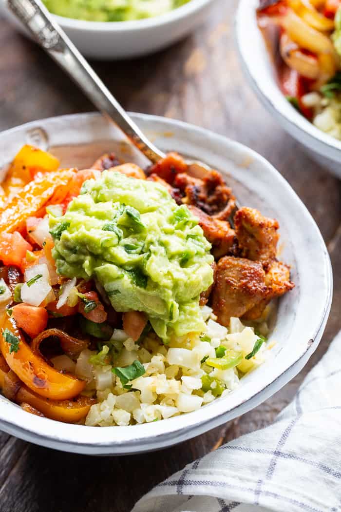 These Paleo Chicken Burrito Bowl are packed with tons of flavor and goodies!  Bite size seasoned chicken thighs, zesty cauliflower rice, pepper and onions plus and easy guac make these bowls healthy, filling, and a family favorite.  Whole30 and keto friendly.