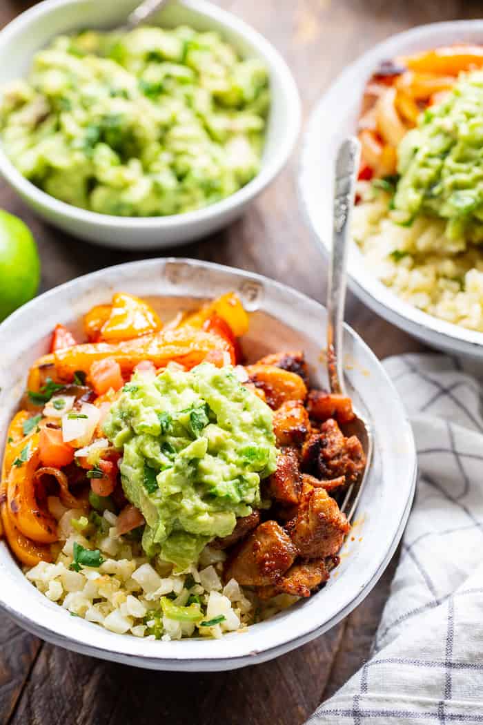 These Paleo Chicken Burrito Bowl are packed with tons of flavor and goodies!  Bite size seasoned chicken thighs, zesty cauliflower rice, pepper and onions plus and easy guac make these bowls healthy, filling, and a family favorite.  Whole30 and keto friendly.