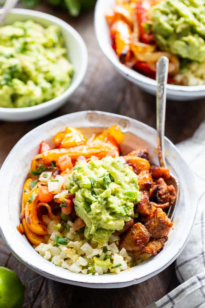 These Paleo Chicken Burrito Bowl are packed with tons of flavor and goodies!  Bite size seasoned chicken thighs, zesty cauliflower rice, pepper and onions plus and easy guac make these bowls healthy, filling, and a family favorite.  Whole30 and keto friendly.