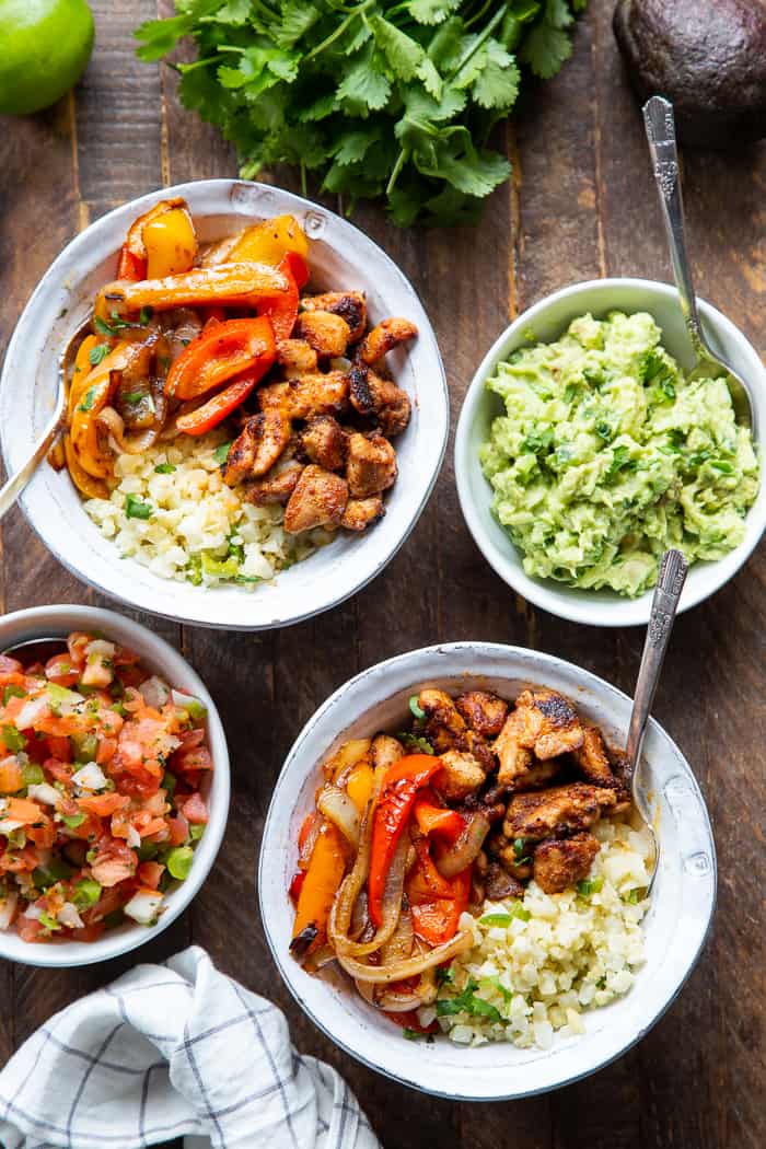 These Paleo Chicken Burrito Bowl are packed with tons of flavor and goodies!  Bite size seasoned chicken thighs, zesty cauliflower rice, pepper and onions plus and easy guac make these bowls healthy, filling, and a family favorite.  Whole30 and keto friendly.