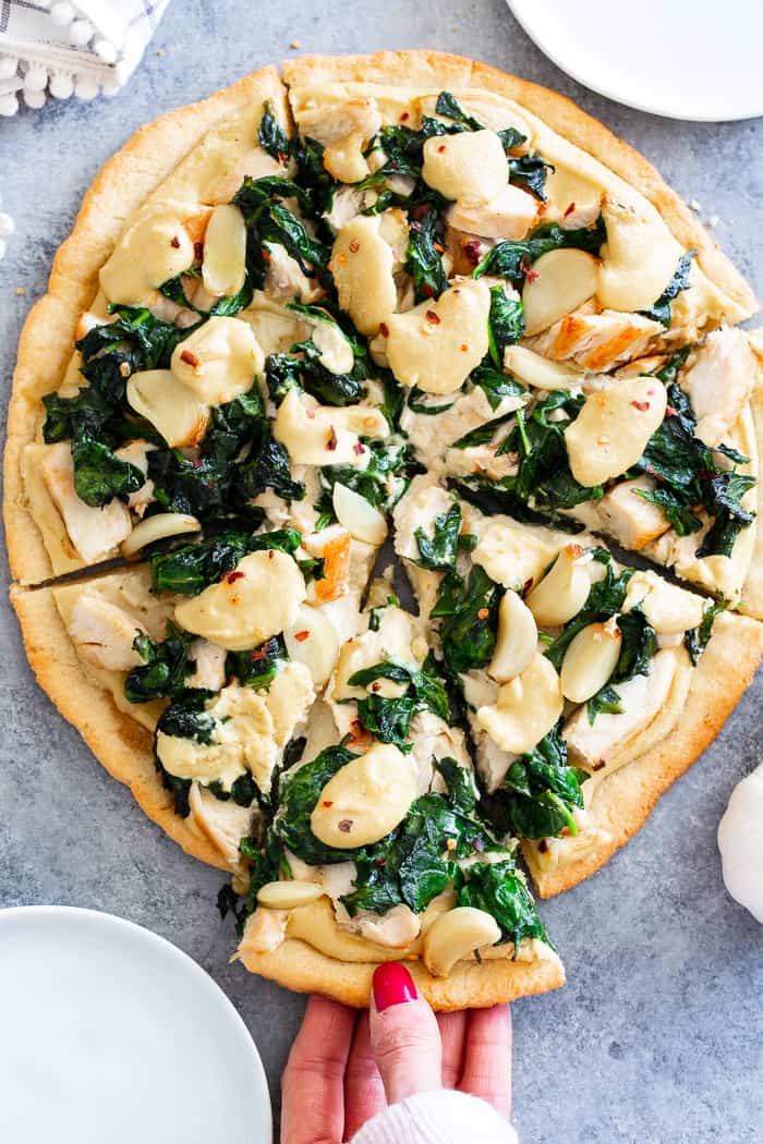 This white pizza has a super tasty roasted garlic cashew cheese sauce with sautéed spinach and chicken, plus more roasted garlic.  Everything is baked on the best easy paleo pizza crust for a fun, filling and delicious paleo and dairy free pizza.