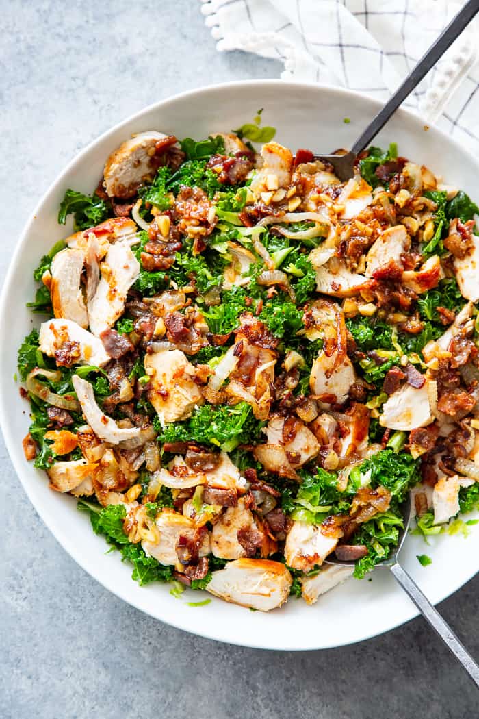 This kale salad is packed to the max with goodies!  Kale is tossed with shredded Brussels sprouts, lots of sweet caramelized onions, crispy bacon and grilled chicken plus a super tasty hot bacon dressing.  It’s dairy free and paleo with both Whole30 and keto options. 