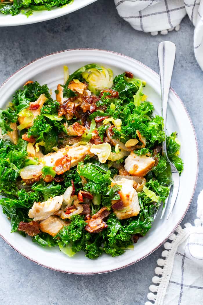This kale salad is packed to the max with goodies!  Kale is tossed with shredded Brussels sprouts, lots of sweet caramelized onions, crispy bacon and grilled chicken plus a super tasty hot bacon dressing.  It’s dairy free and paleo with both Whole30 and keto options. 