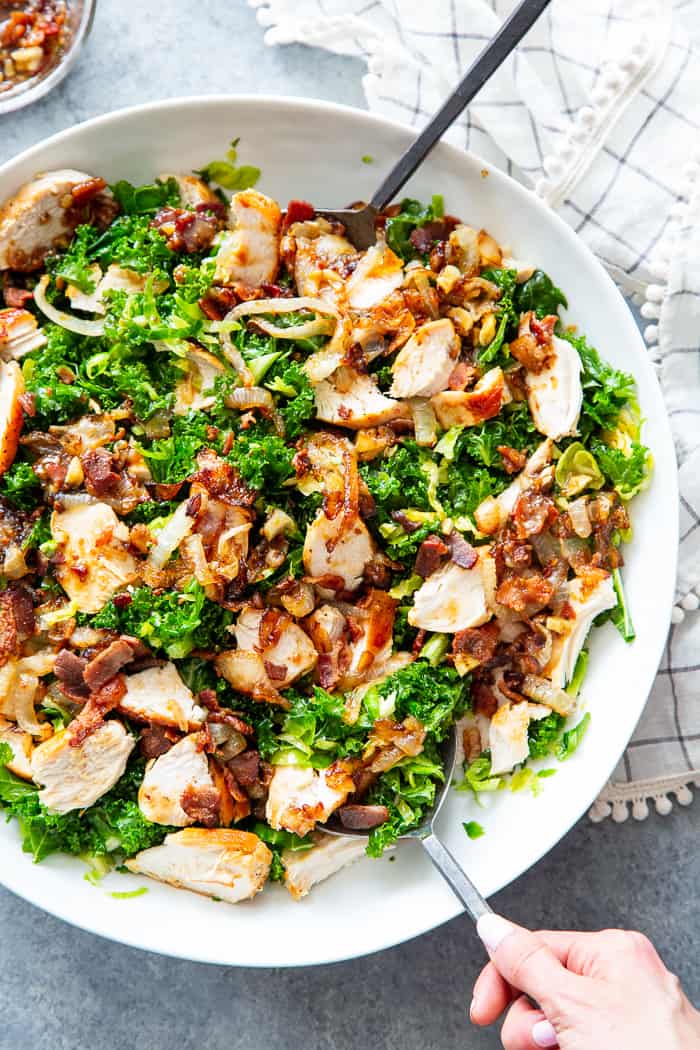 This kale salad is packed to the max with goodies!  Kale is tossed with shredded Brussels sprouts, lots of sweet caramelized onions, crispy bacon and grilled chicken plus a super tasty hot bacon dressing.  It’s dairy free and paleo with both Whole30 and keto options. 