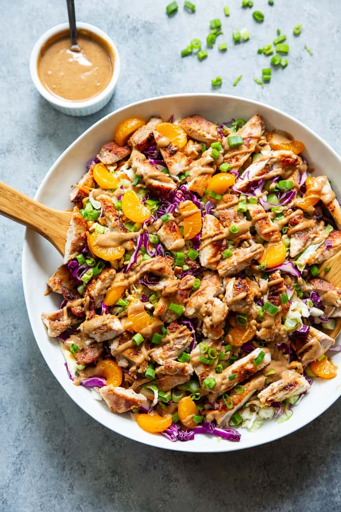 Chinese chicken salad in a bowl aside scattered scallions and a dish of salad dressing