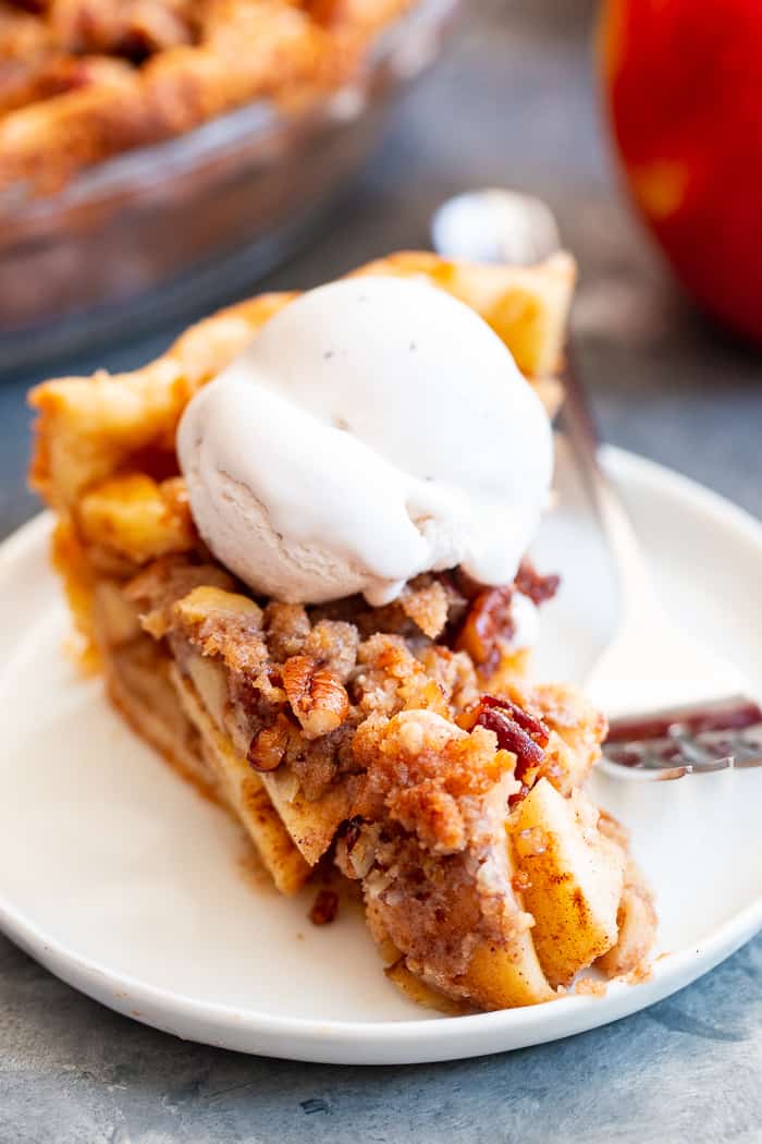 a slice of apple pie with a scoop of white ice cream on top on a white plate