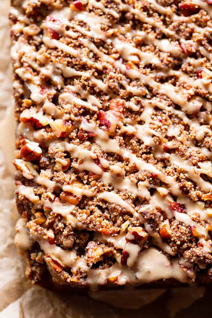 a slab of pumpkin cake with pecan crumble topping and a generous drizzle of a light brown glaze