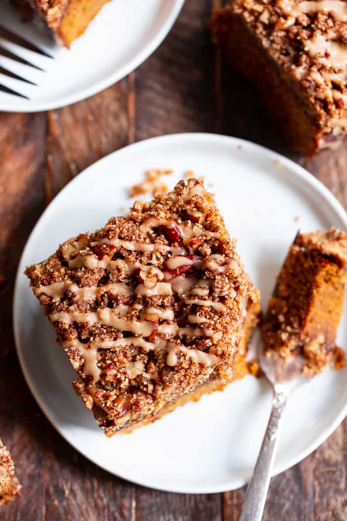 a square slice of pumpkin coffee cake with pecan crumb topping and glaze drizzle on a white plate