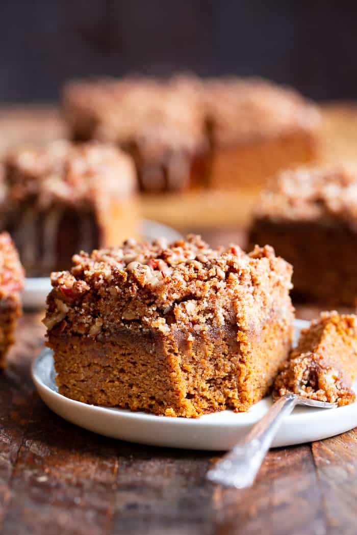 a slice of brown cake with a crumb topping on a white plate with a fork to the side