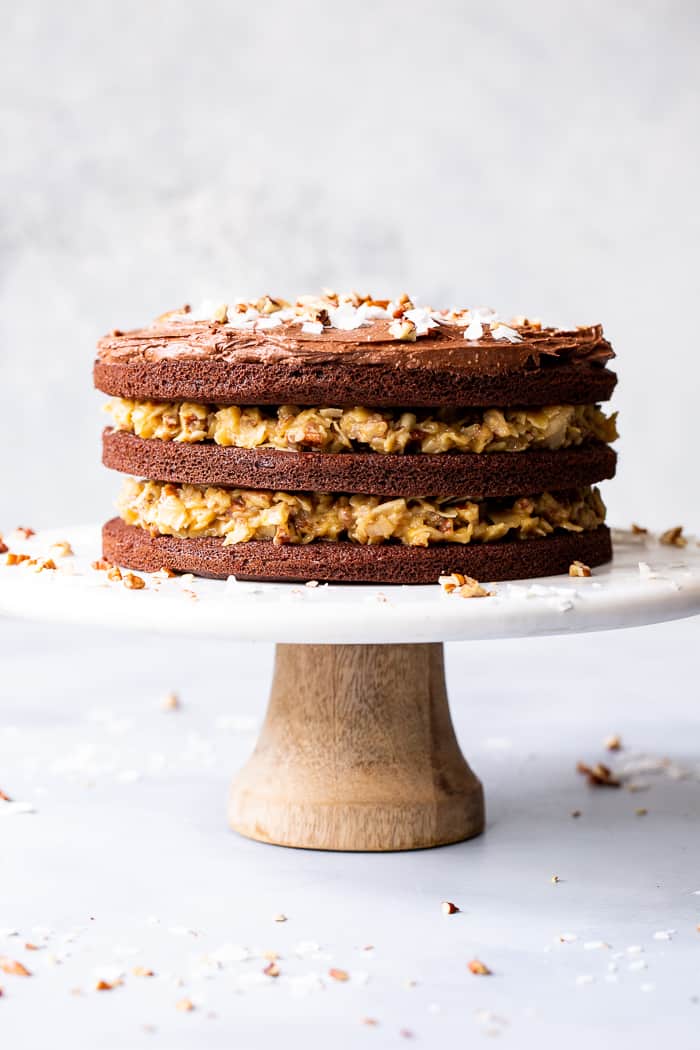 This rich Paleo German Chocolate Cake has a classic coconut pecan filling between tender grain free chocolate cake layers, and is topped with a dairy-free, refined sugar free chocolate frosting.  A showstopper for any gathering, this healthy German Chocolate Cake will become a family favorite!