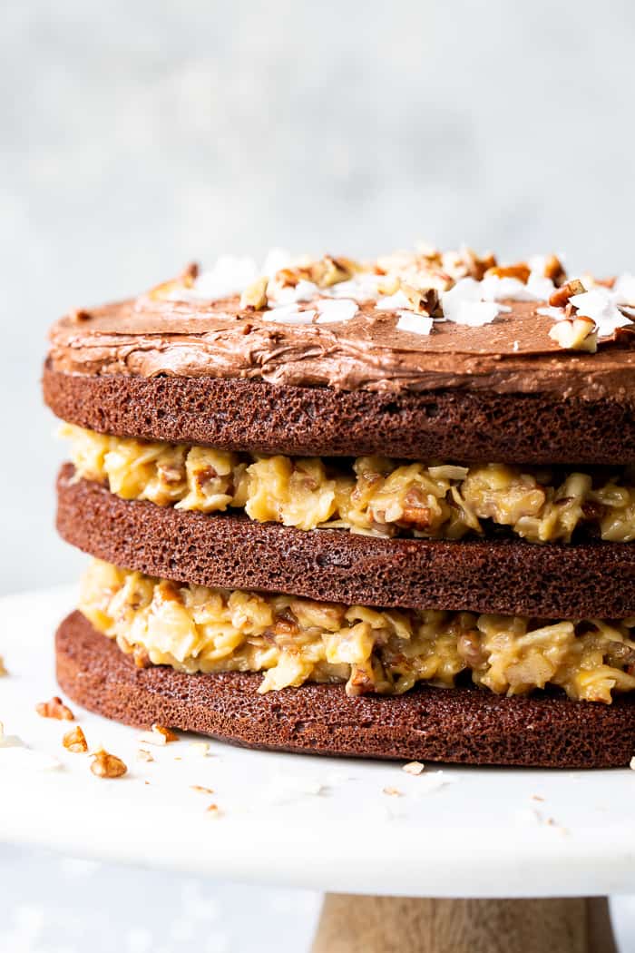 This rich Paleo German Chocolate Cake has a classic coconut pecan filling between tender grain free chocolate cake layers, and is topped with a dairy-free, refined sugar free chocolate frosting.  A showstopper for any gathering, this healthy German Chocolate Cake will become a family favorite!