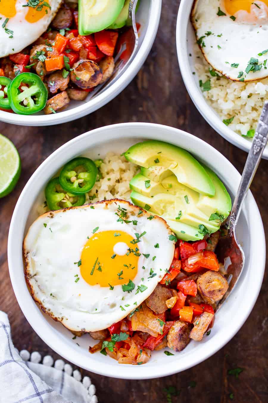 These Paleo breakfast burrito bowls are loaded with goodies!  Savory No Antibiotics Ever All Natural Golden Brown Chicken Sausage, peppers, onions, and seasoned cauliflower rice topped with sliced avocado and eggs. These delicious breakfast bowls are low carb, Whole30 compliant and super easy to throw together!