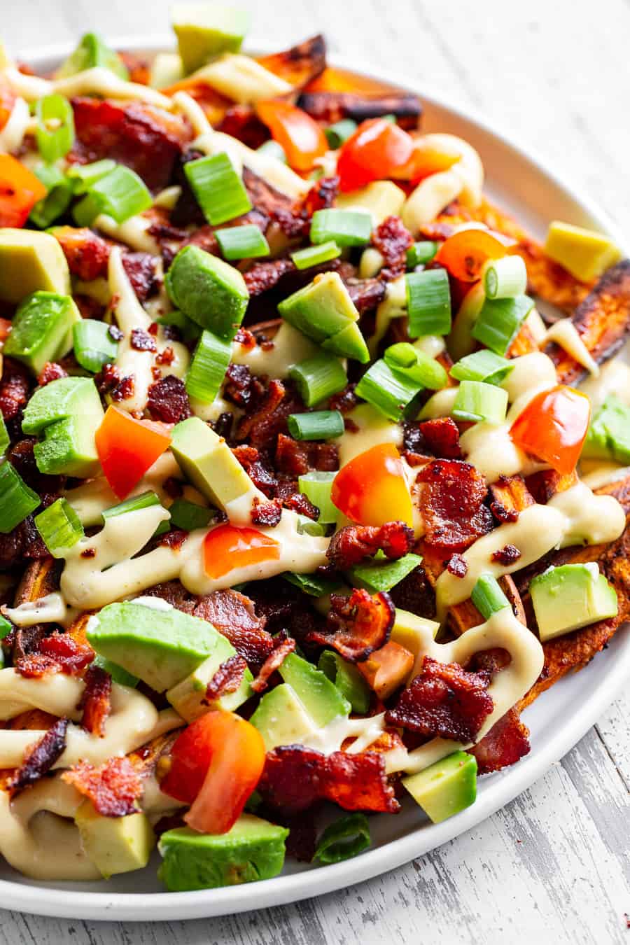 These loaded sweet potato fries are easy to make and packed with goodies! Sweet potato fries are baked crispy and topped with plenty of No Sugar Hickory Smoked Bacon from @jonesdairyfarm, dairy-free cheese sauce, green onions, avocado and tomatoes. This fun meal or appetizer is kid approved, paleo, Whole30 compliant and seriously tasty! #Whole30 #paleo #cleaneating #AD