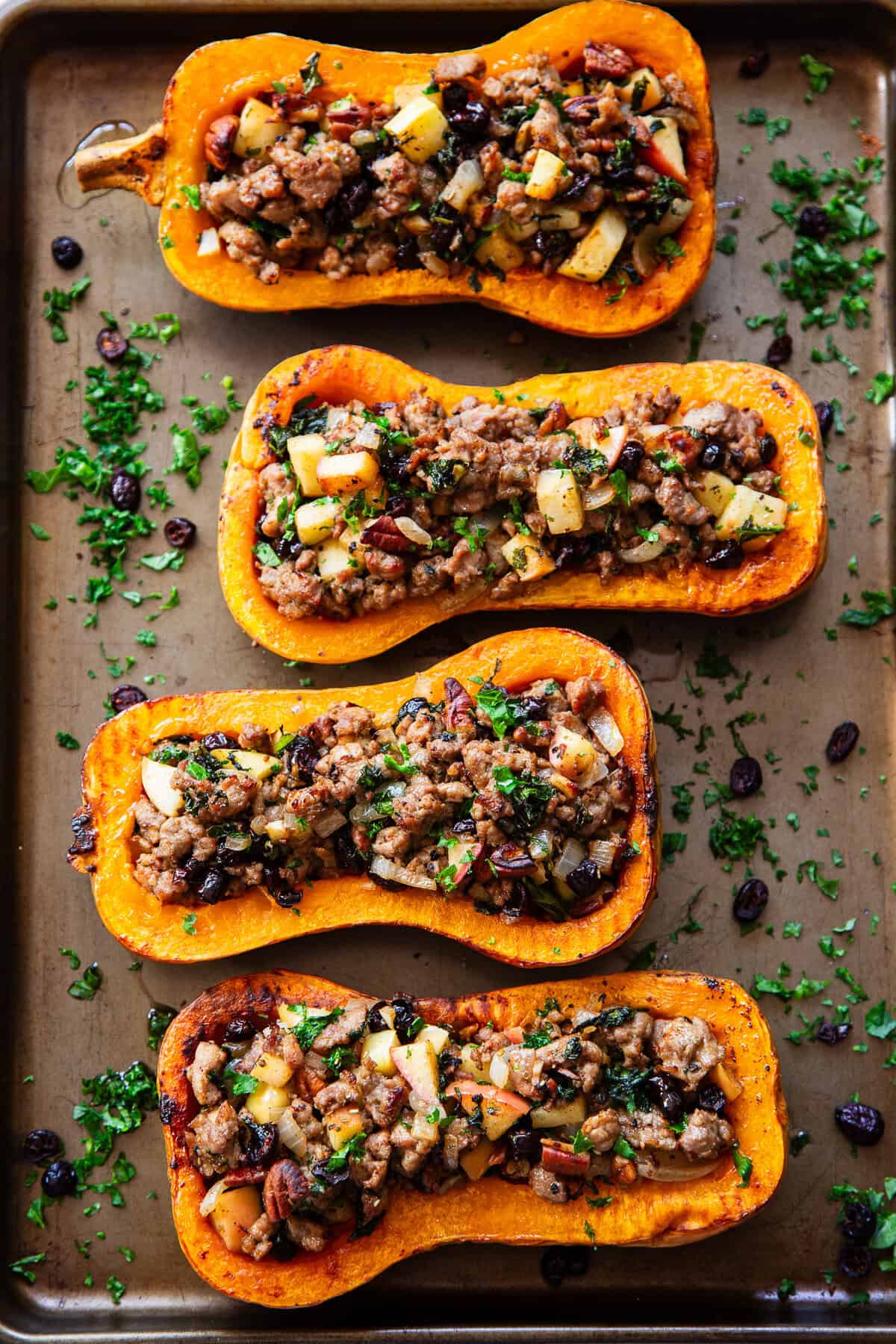 Overhead view of roasted stuffed butternut squash is filled with a savory-sweet mixture of Italian sausage, apples, cranberries, kale, pecans and fresh herbs.