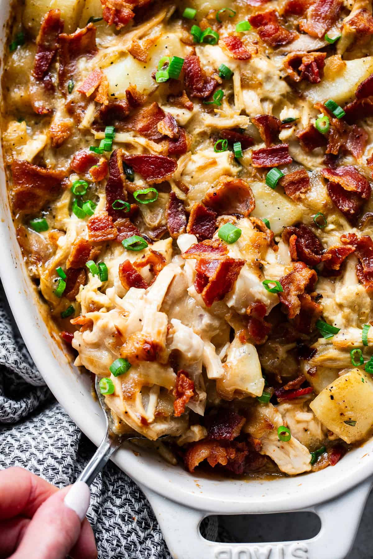 Spoon serving creamy chicken potato casserole with bacon and potatoes, close up.