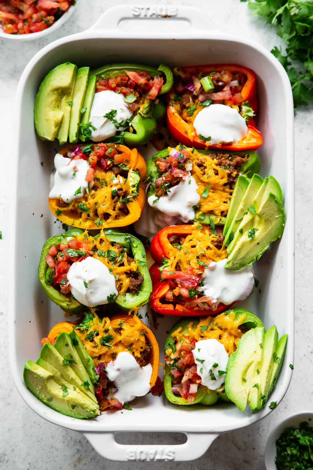 These Paleo Taco Stuffed Peppers are super easy to make and packed with goodies! Bell peppers are filled with the best taco meat and topped with vegan cheese, baked, and topped with all your favorites like fresh pico de Gallo, avocado and dairy free sour cream. Paleo, dairy free and keto friendly. #paleo #keto #cleaneating #lowcarb