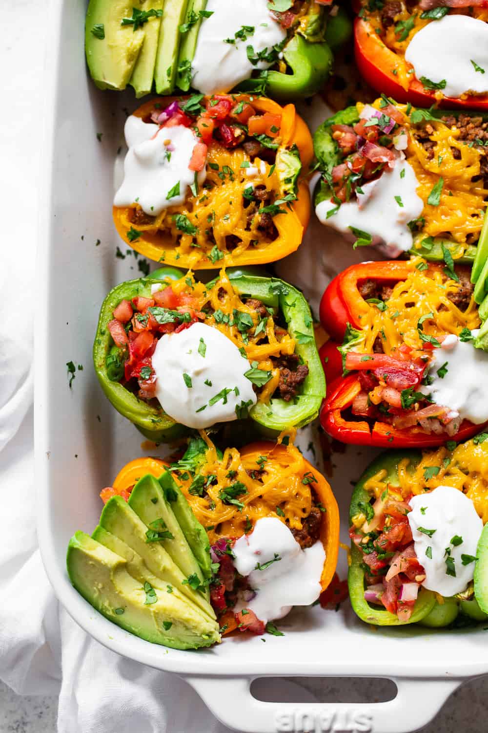 These Paleo Taco Stuffed Peppers are super easy to make and packed with goodies! Bell peppers are filled with the best taco meat and topped with vegan cheese, baked, and topped with all your favorites like fresh pico de Gallo, avocado and dairy free sour cream. Paleo, dairy free and keto friendly. #paleo #keto #cleaneating #lowcarb