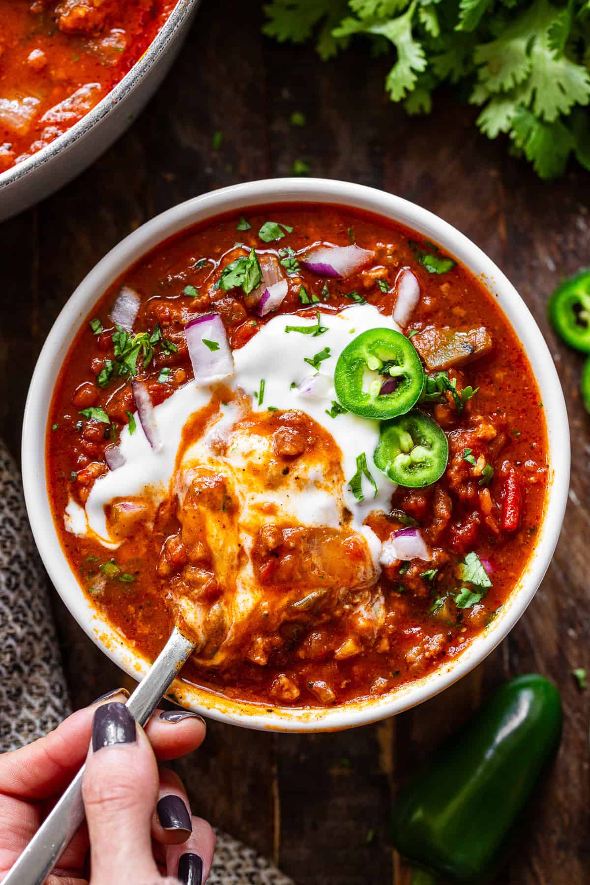 Spoonful of hearty pumpkin chili lifted from a bowl with sour cream and jalapeños