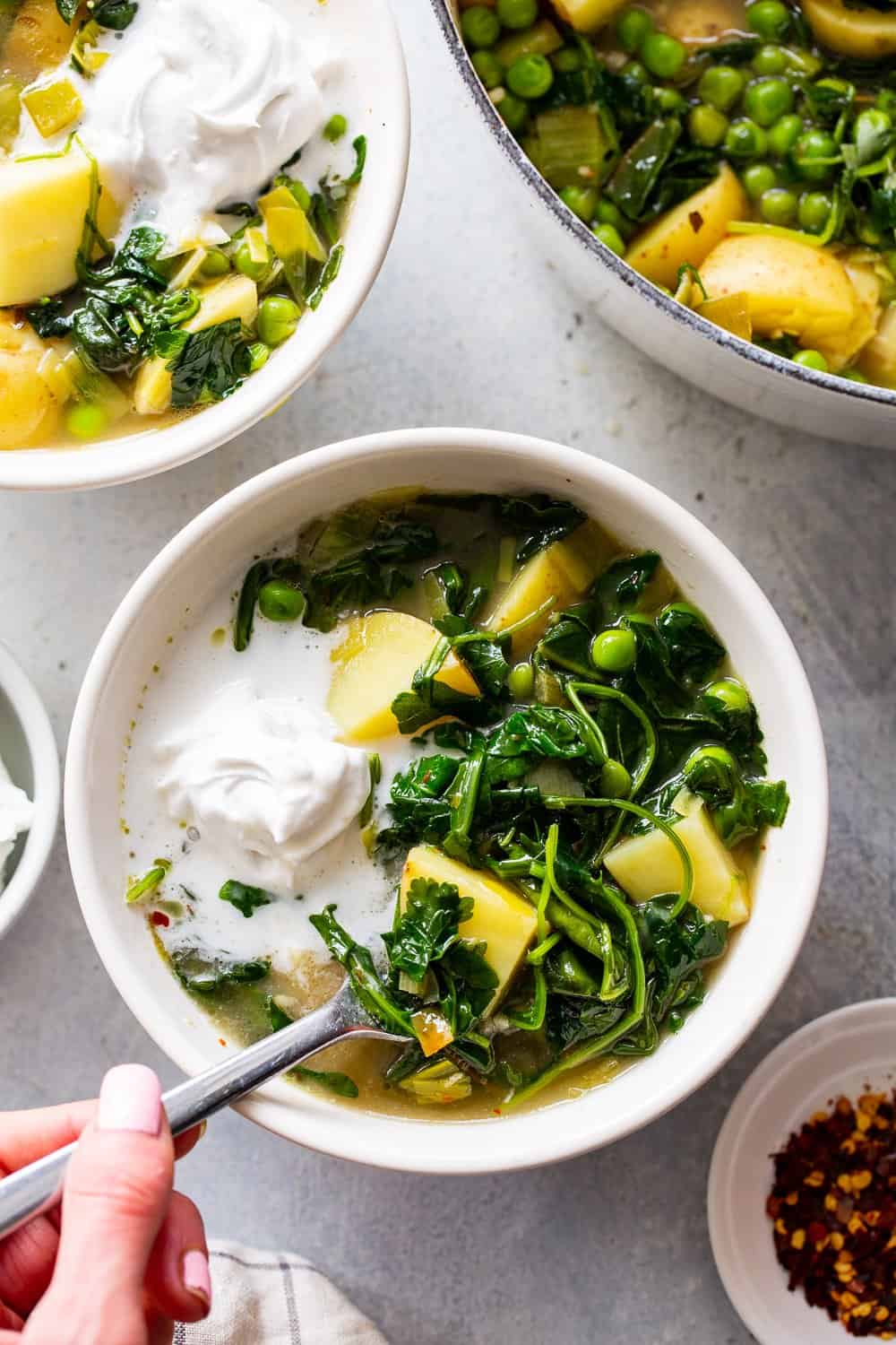 This chunky spring greens soup is full of flavor, good fats and healthy carbs. Golden potatoes, peas, spring veggies and an easy homemade dairy free sour cream make it hearty, healthy and so delicious. #paleo #whole30 #cleaneating