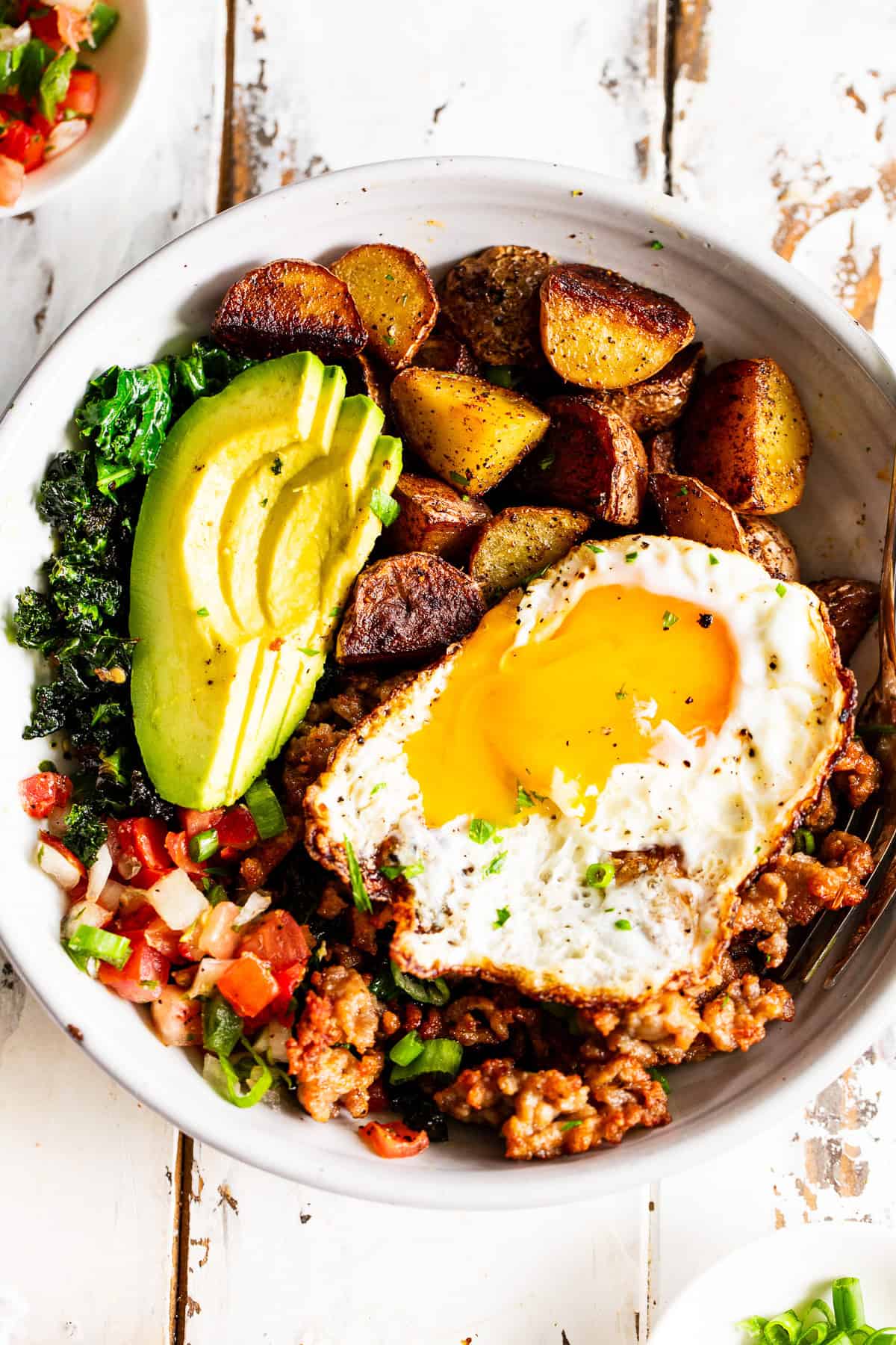 high protein savory breakfast bowl with baby potatoes, greens, sausage, avocado and fried egg