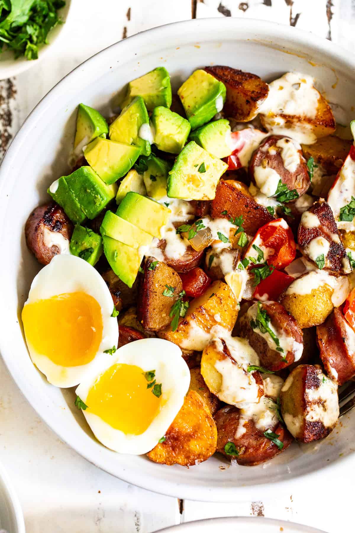 High protein chicken sausage breakfast bowl with crispy potatoes, jammy eggs, avocado and salsa verde sauce.