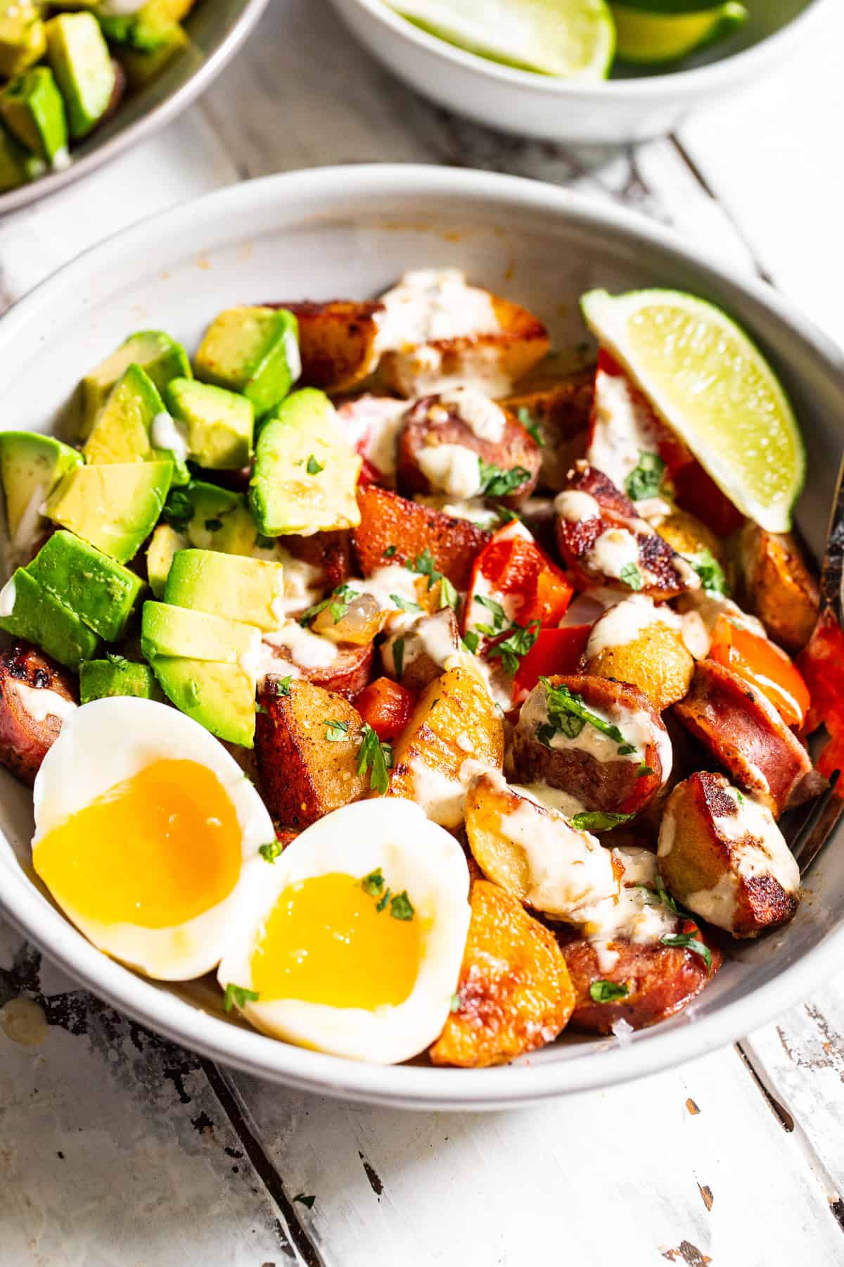 High protein chicken sausage breakfast bowl with crispy potatoes, jammy eggs, avocado and salsa verde sauce.