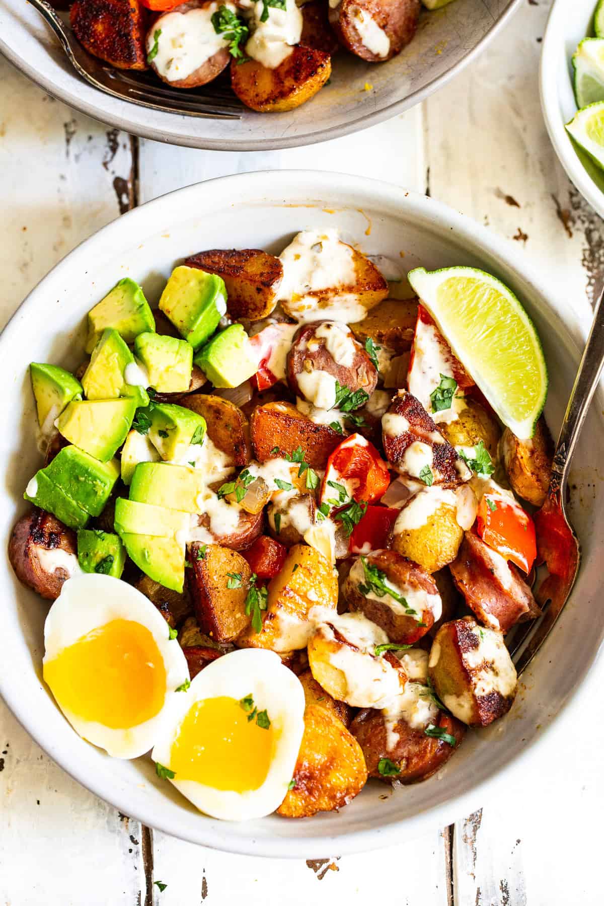 High protein chicken sausage breakfast bowl with crispy potatoes, jammy eggs, avocado and salsa verde sauce.