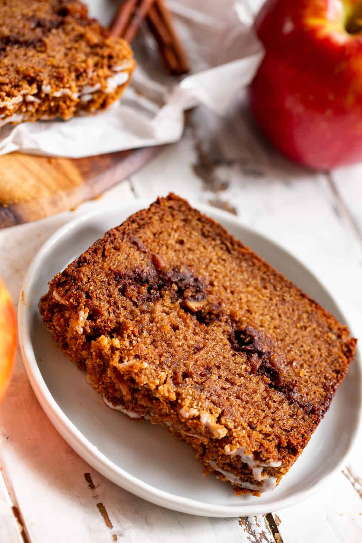 Thick slice of apple cinnamon swirl bread served on a white plate with fresh apples