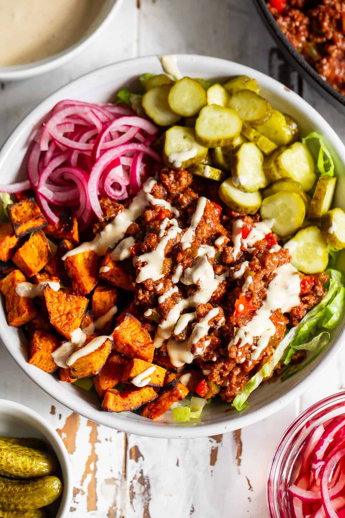 Healthy sloppy joe bowl with seasoned ground beef, roasted sweet potatoes, lettuce, pickles and red onion