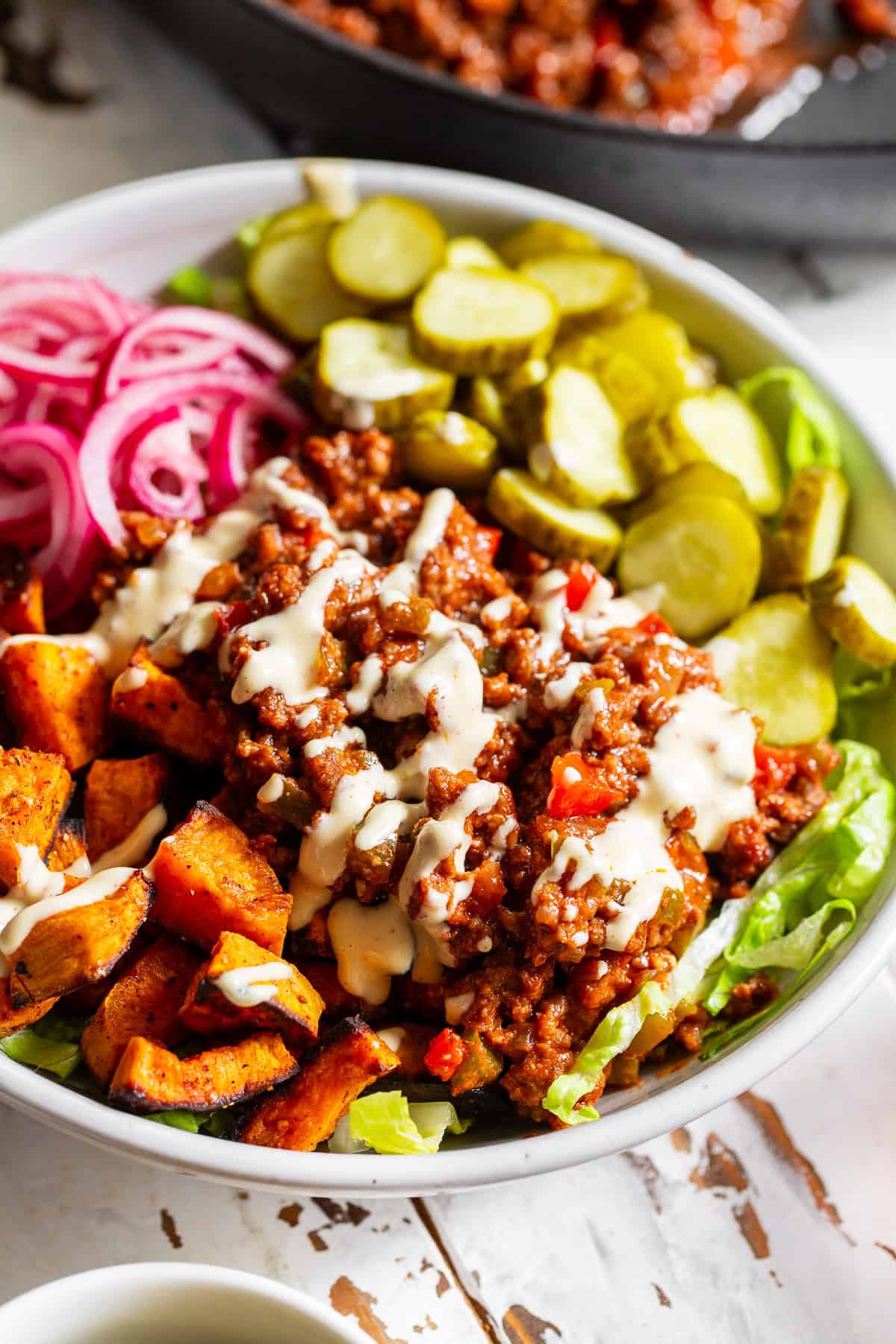 Healthy sloppy joe bowl with seasoned ground beef, roasted sweet potatoes, lettuce, pickles and red onion