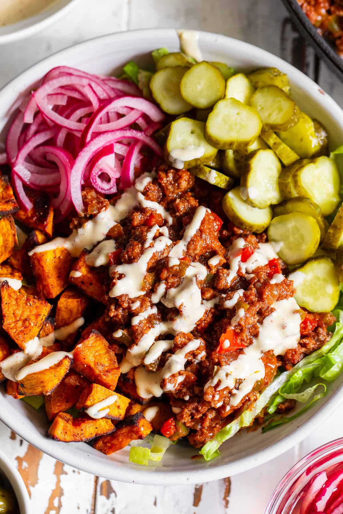 Healthy sloppy joe bowl with seasoned ground beef, roasted sweet potatoes, lettuce, pickles and red onion