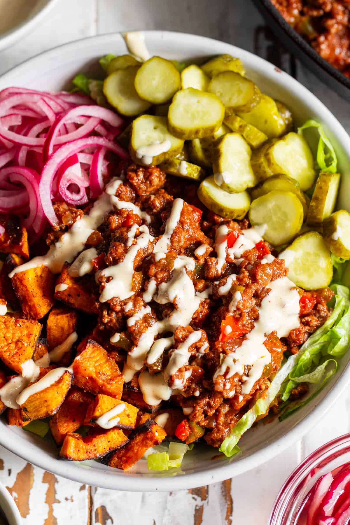 Healthy sloppy joe bowl with seasoned ground beef, roasted sweet potatoes, lettuce, pickles and red onion