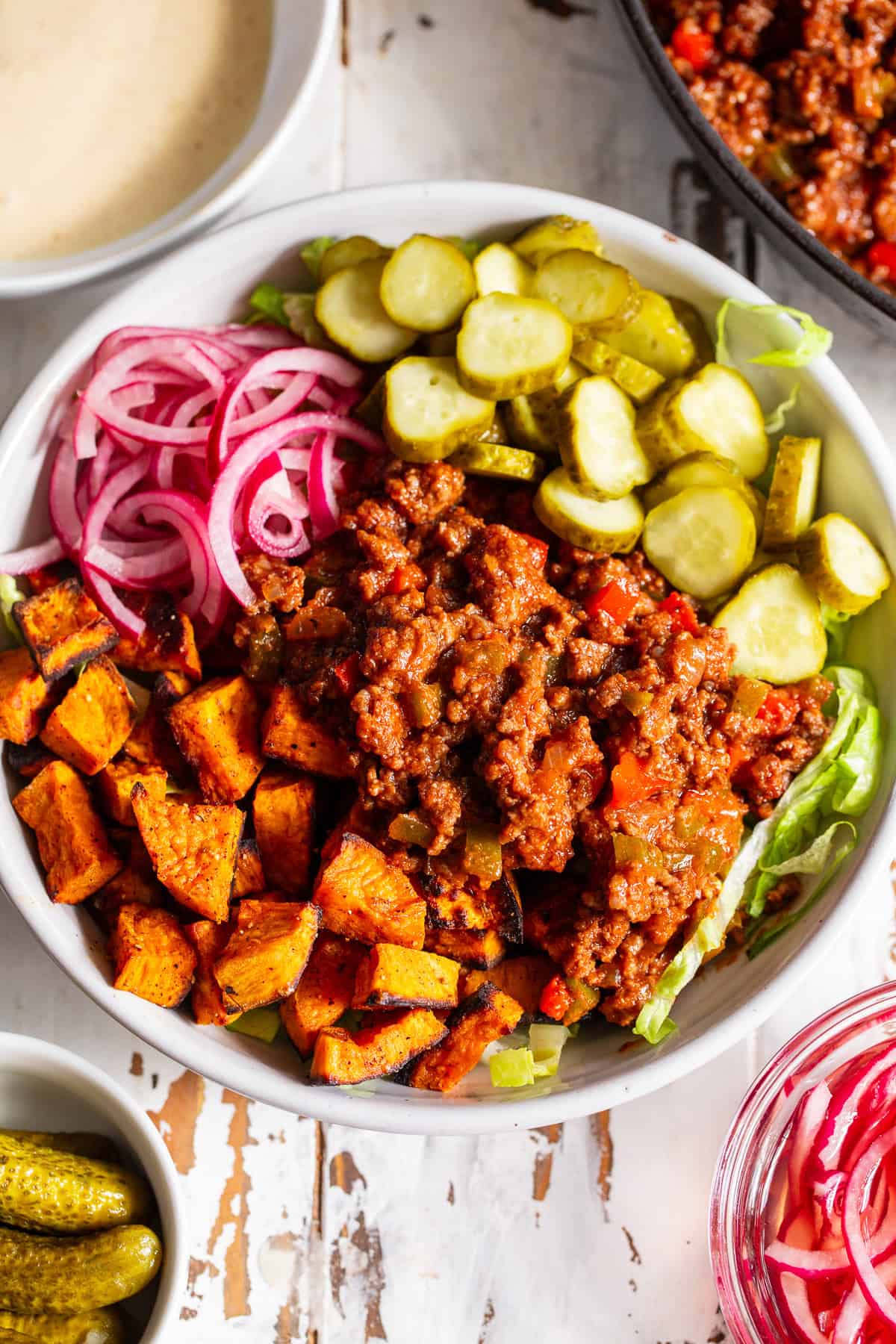 Healthy sloppy joe bowl with seasoned ground beef, roasted sweet potatoes, lettuce, pickles and red onion