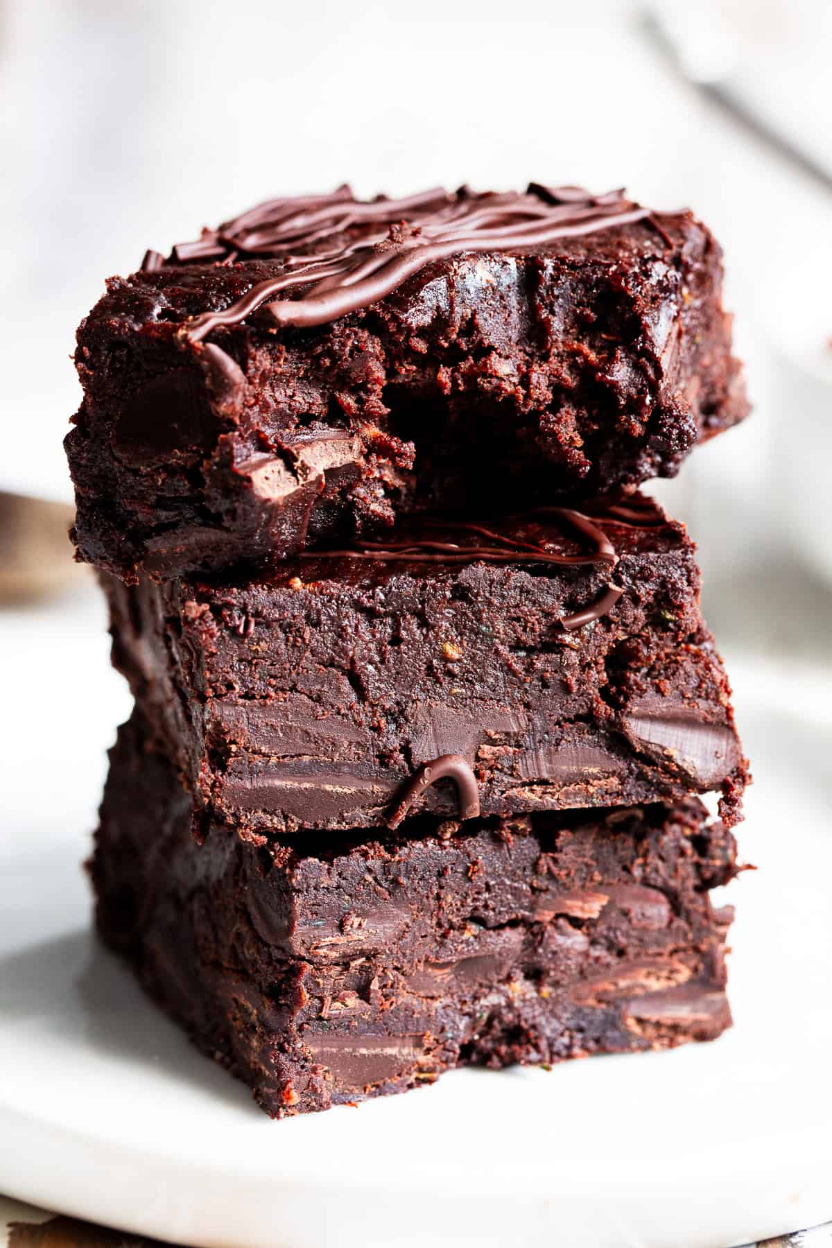 Healthy zucchini brownies stacked on a white plate showing the fudgy chocolate center