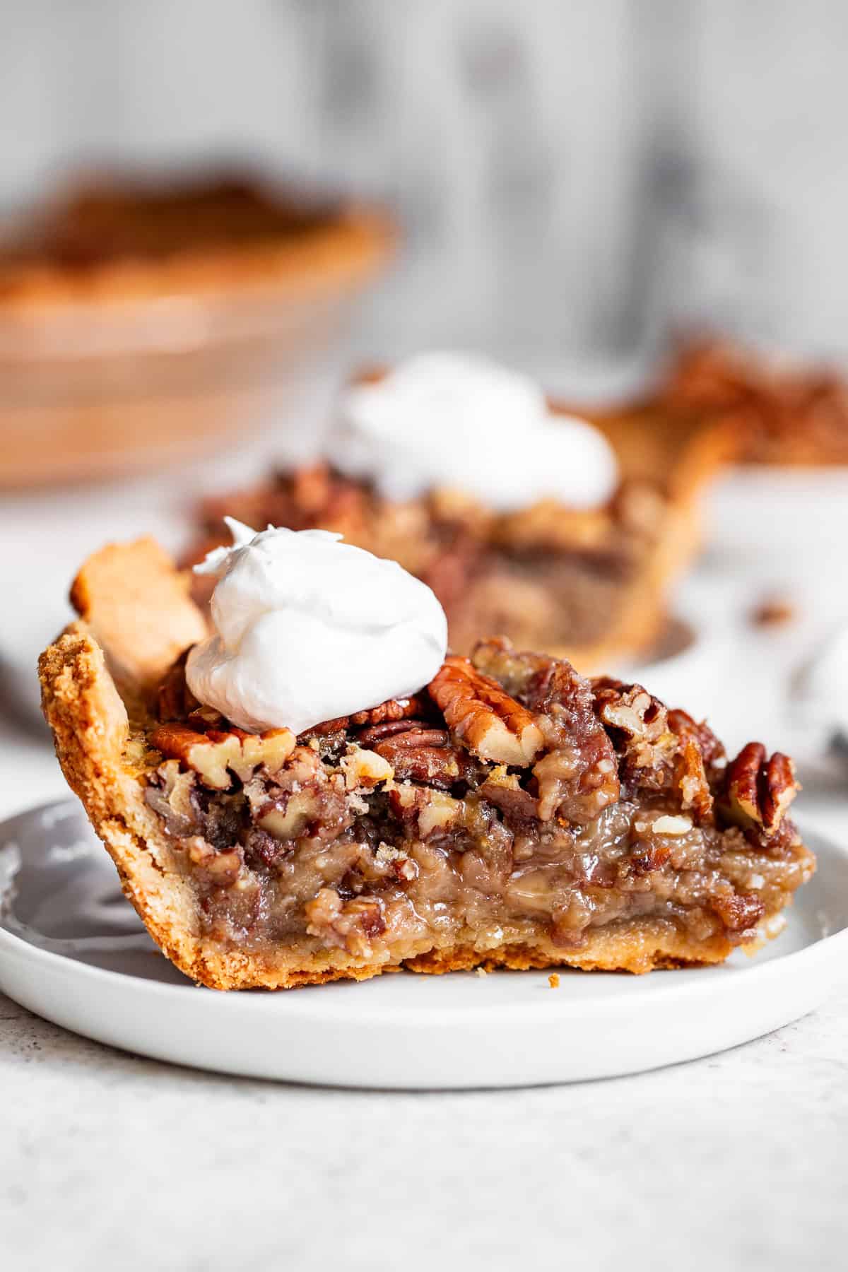 Slice of paleo pecan pie with maple filling and whipped cream on a white plate.