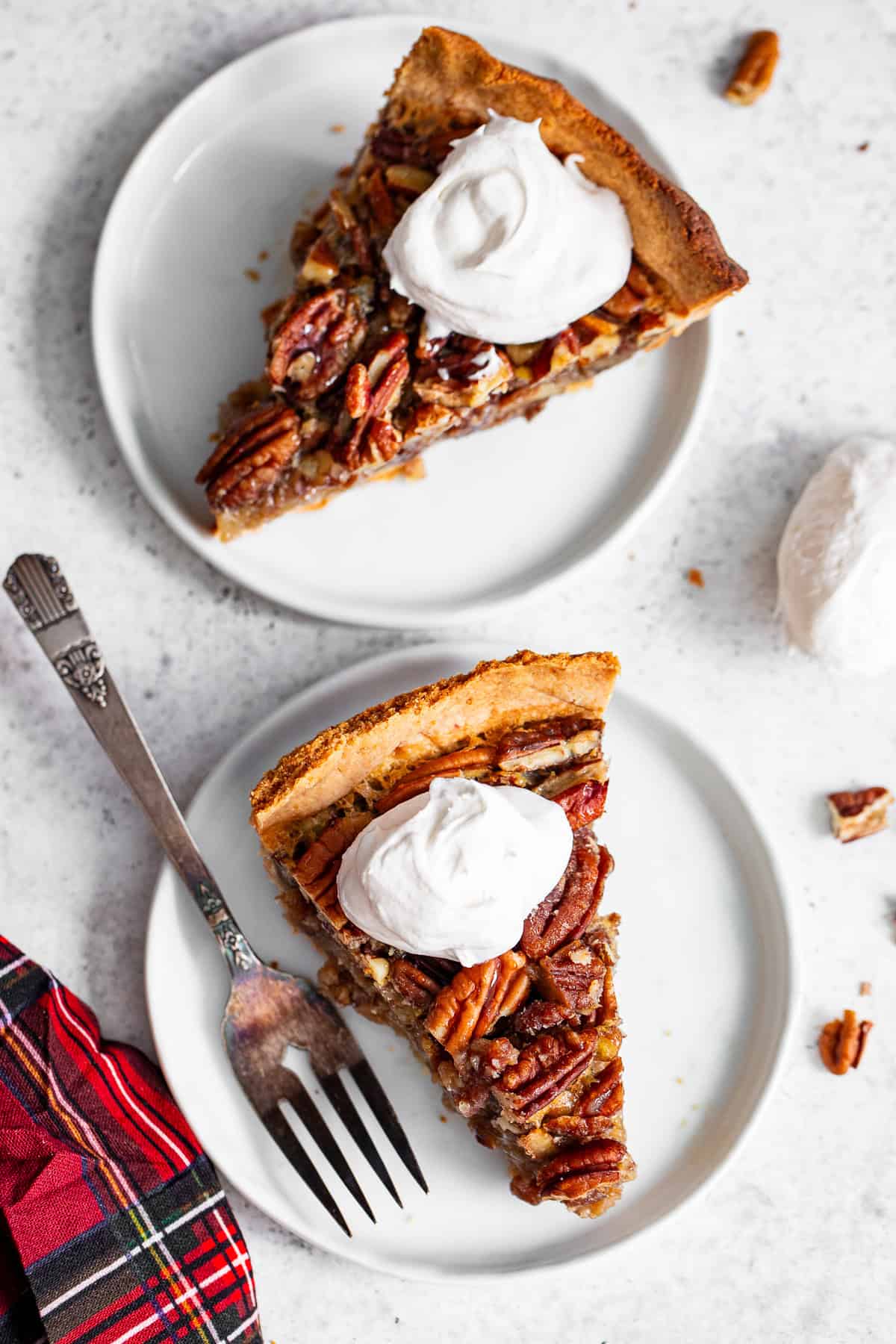 2 slices of paleo pecan pie with maple filling and whipped cream white plates.