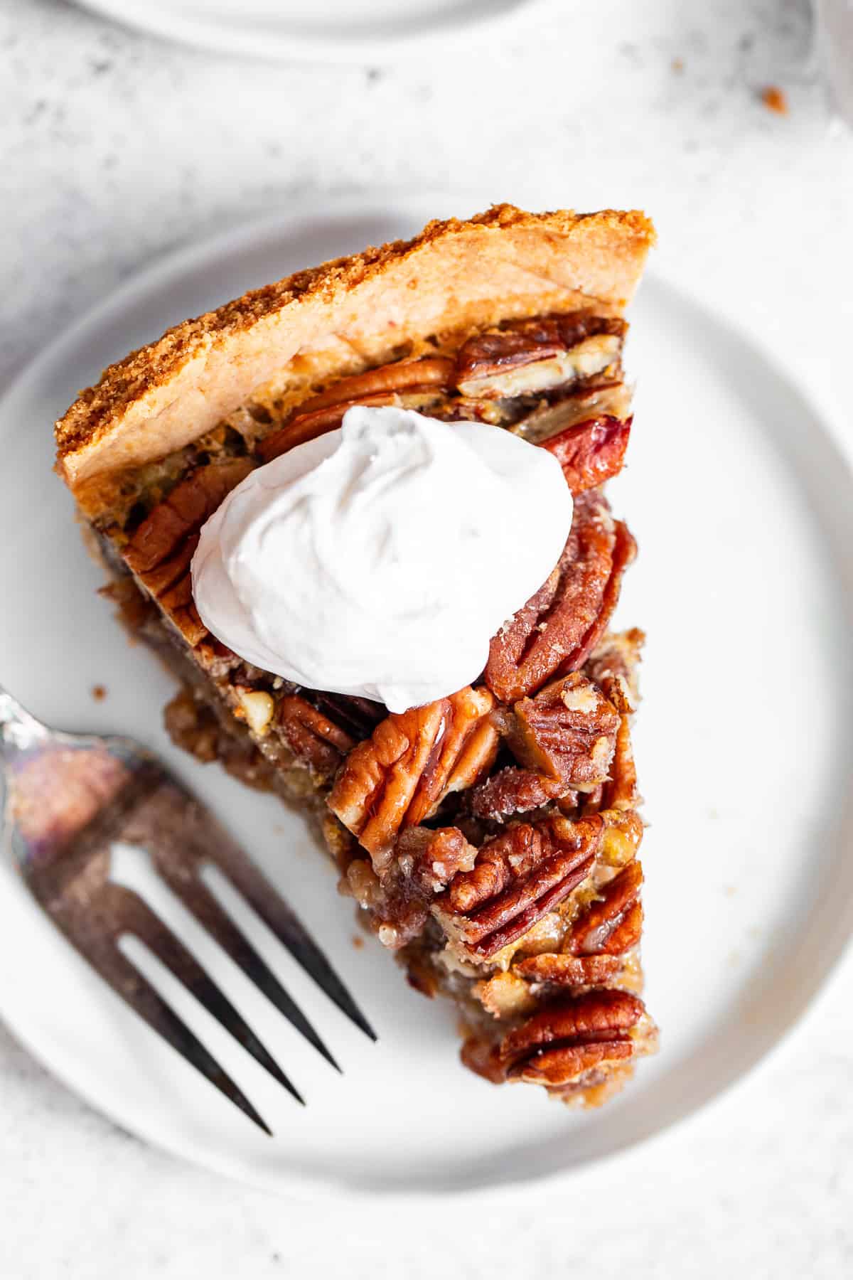Slice of paleo pecan pie with maple filling and whipped cream on a white plate.