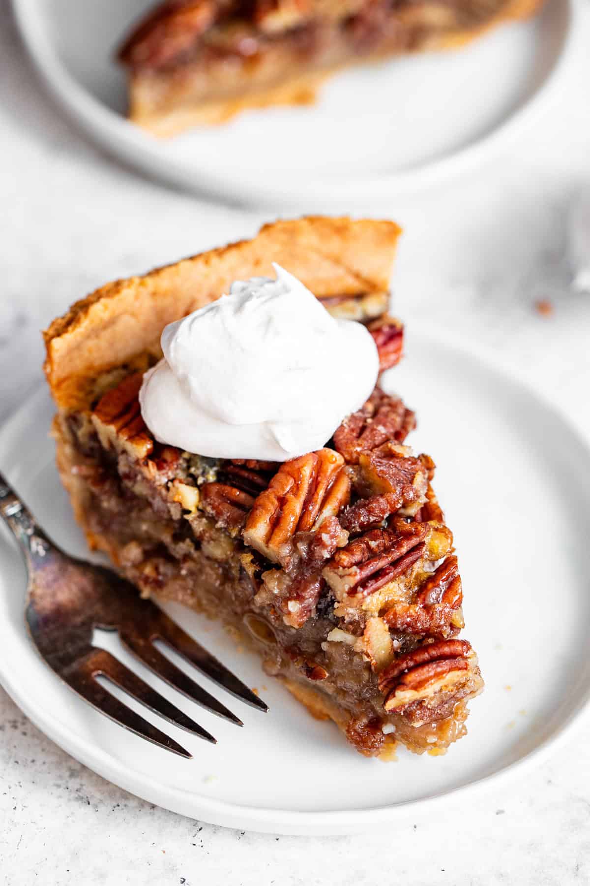 Slice of paleo pecan pie with maple filling and whipped cream on a white plate.